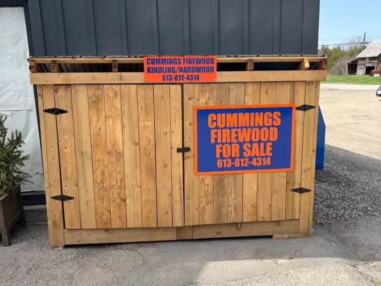 A wooden roadside stand with a Cummings Firewood for sale sign